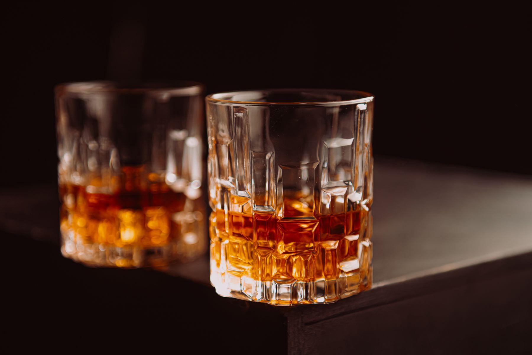 Two cut-crystal whisky tumblers catching warm light on a dark table
