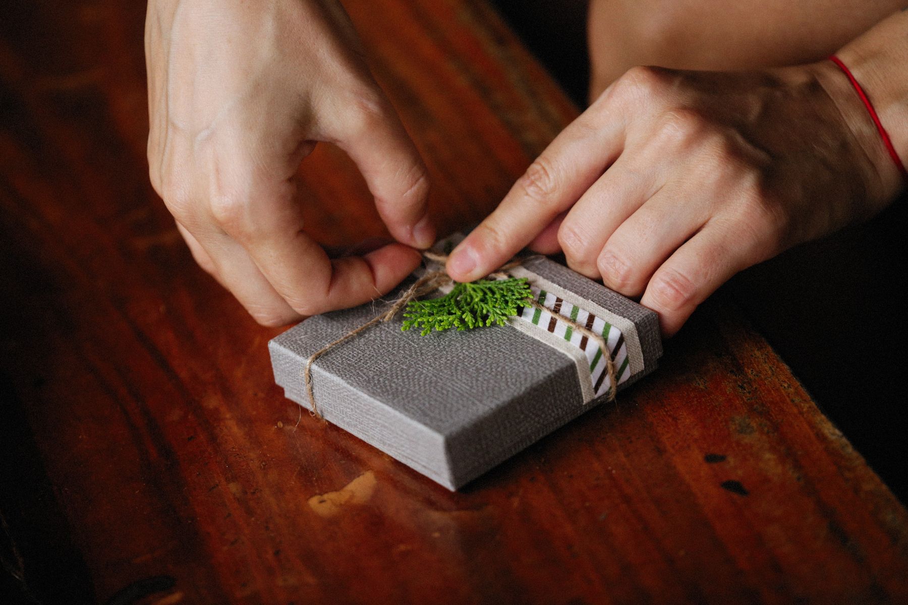 Hands finishing a small grey presentation box with twine and a sprig of greenery