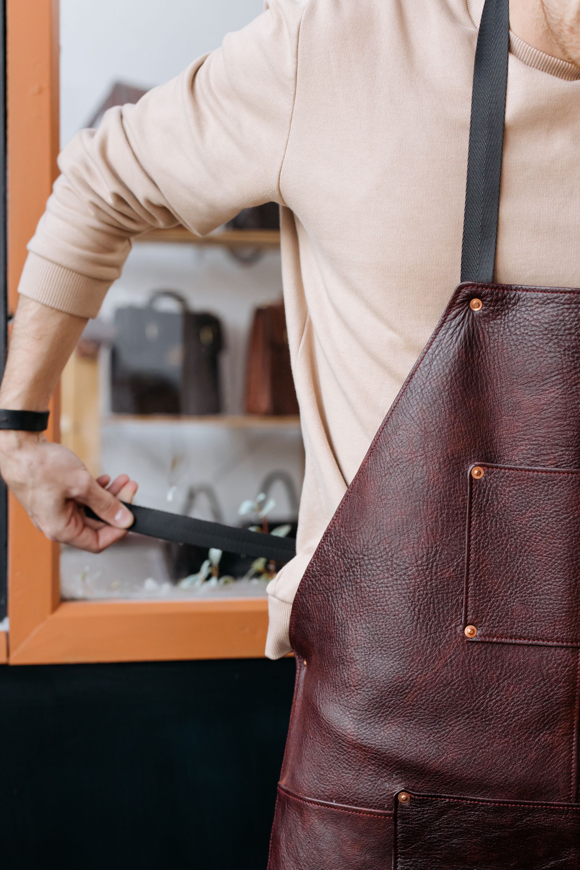 An artisan fastening the strap of a deep burgundy leather apron