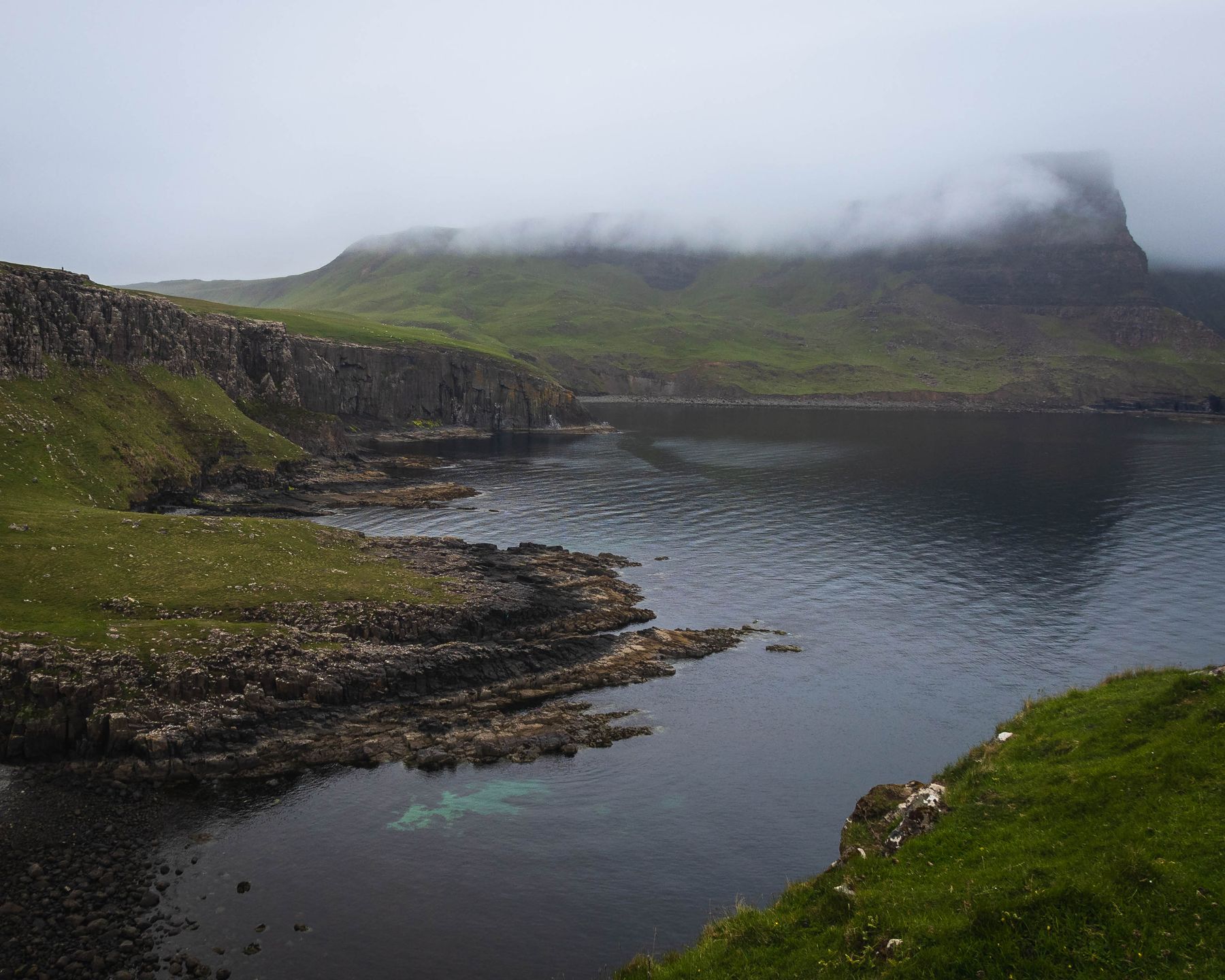 Misty green cliffs falling into a quiet Scottish sea loch