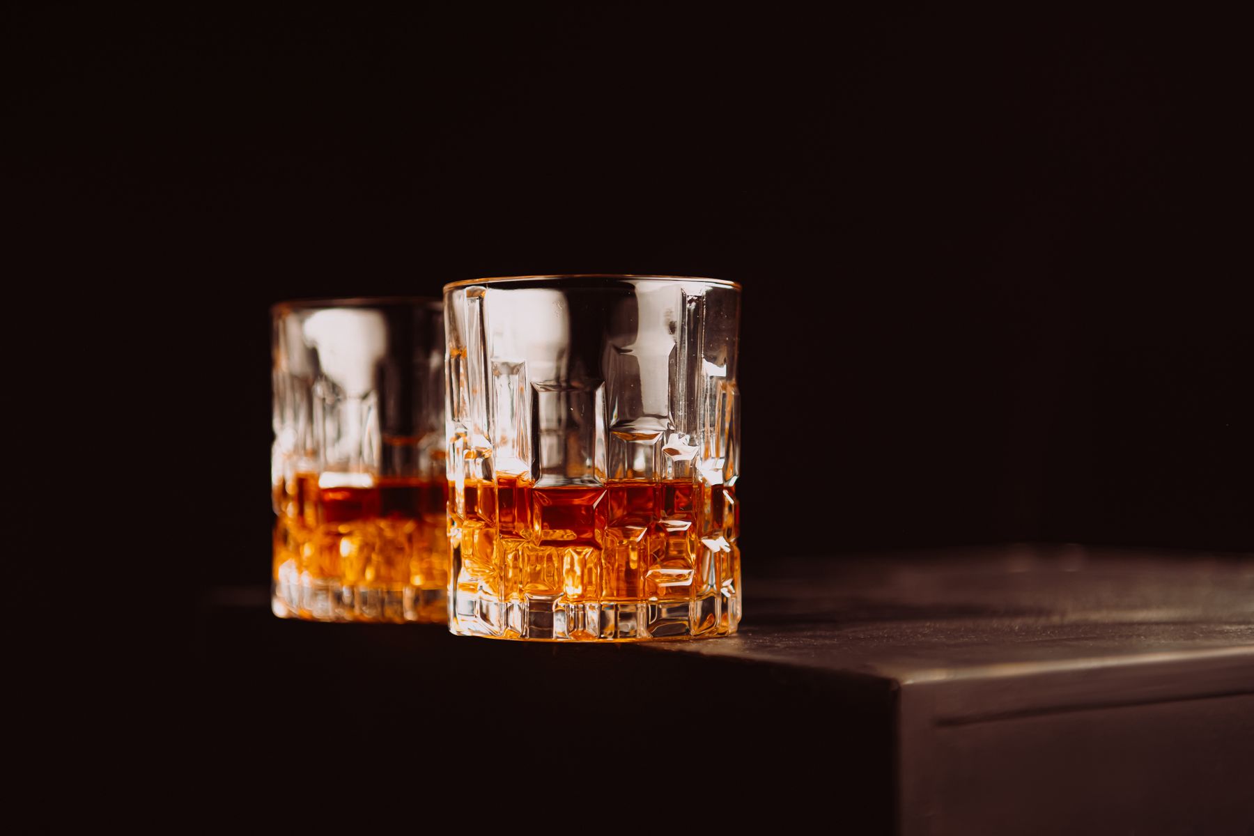 Two whisky glasses on a dark reflective surface